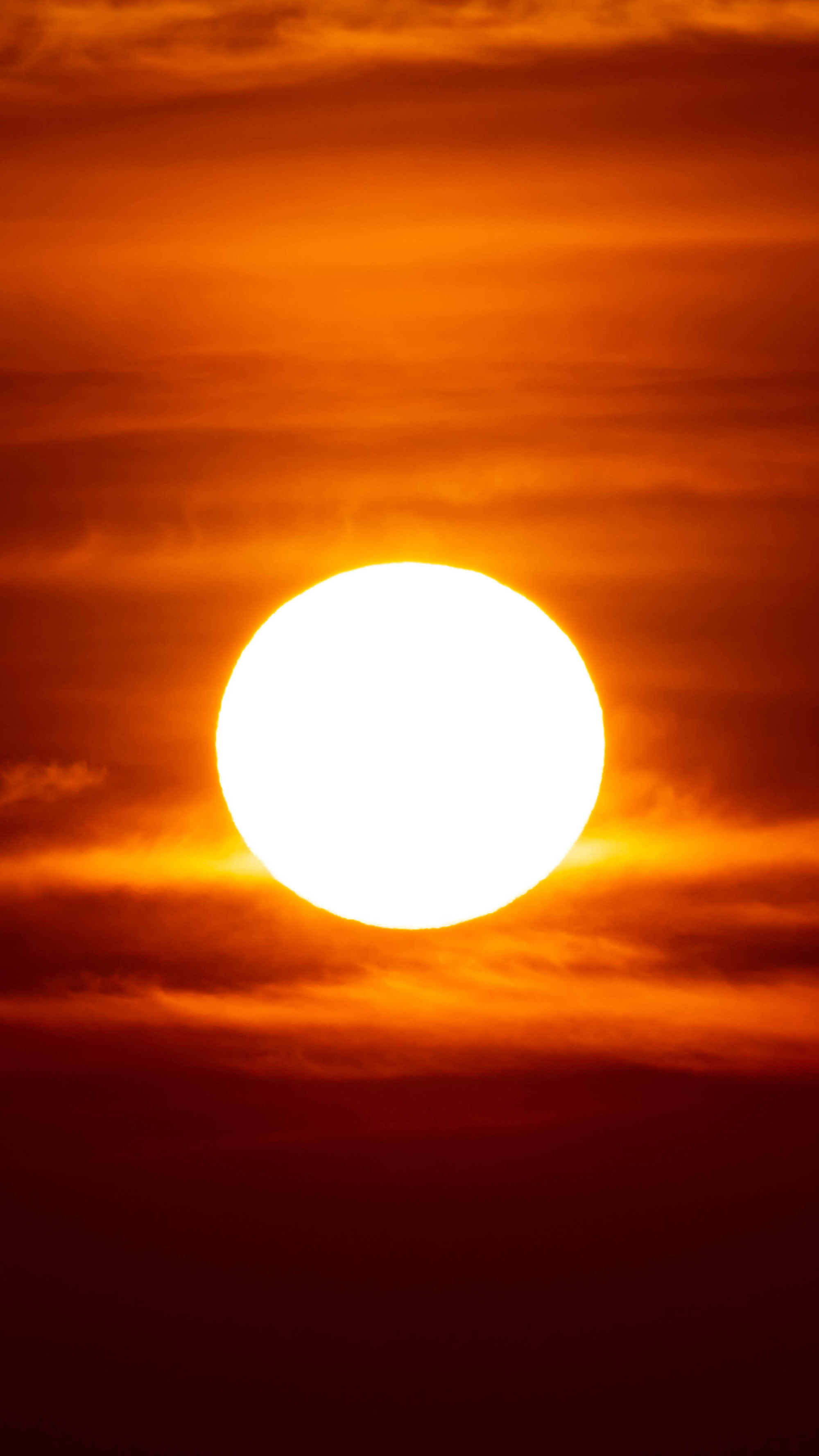 An image of a deep orange sun amongst a set of clouds.